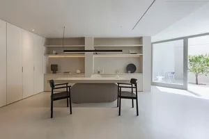 A modern minimalist office with a concrete desk, black chairs, and a sleek, white storage unit with built-in shelves.