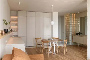 Modern minimalist kitchen featuring a round wooden table, wooden chairs, and white cabinets with glass block wall.