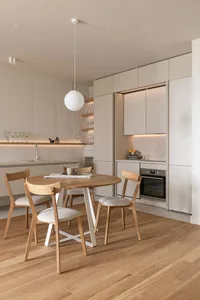 Modern residential kitchen featuring a round wooden table with white chairs, white countertops, and minimalist design element