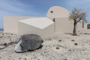 Modern building exterior featuring beige sandstone walls and a large rock in the foreground.