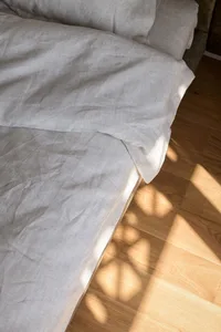 A neatly made bed with minimalist bedding on a wooden floor.