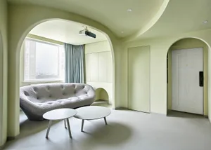 A modern lounge area with a curved sofa, two round tables, and a projector mounted on the ceiling.