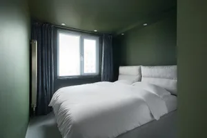 A clean, minimalist bedroom with a large bed, white bedding, and natural light coming through the window.