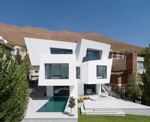 Modern minimalist house with white concrete walls, large glass windows, and a landscaped yard.