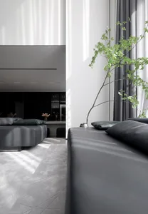 Modern minimalist living room with black leather sofas, glass coffee table, and wooden floor.