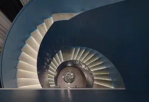 A modern, industrial-style staircase with wooden steps and a metal guardrail, illuminated by a hanging lamp in the center.