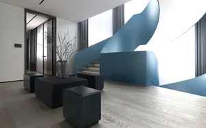 A modern living room with a blue staircase, black ottomans, and a white wooden floor.
