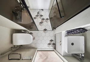 Modern minimalist bathroom with white hexagonal tiles on the floor and walls, a white vanity sink, and a glass-enclosed showe
