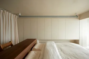 A minimalist bedroom with a textured wooden bed frame and neutral-colored bedding against a white wall.