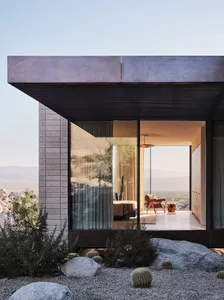 A modern living room with concrete walls and large windows, showcasing minimalist design and a connection to the outdoors.