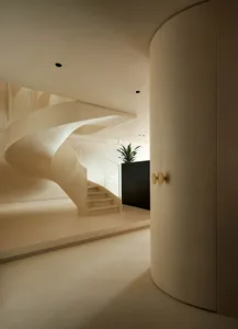 A sleek, modern staircase made of concrete with a spiral design, featuring a wall-mounted light fixture and a plant in the ba