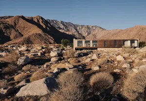 現代極簡住宅搭配大型窗戶與金屬包覆，背景為崎嶇山景。