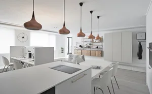 A modern office kitchen with white materials and minimalist design, featuring a white countertop, pendant lights, and a white