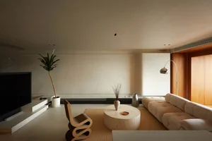 A living room featuring a modern, neutral-toned interior design with a cozy sofa, side table, and a tall plant.