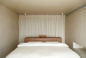 A minimalist bedroom featuring a wooden headboard and curtain.
