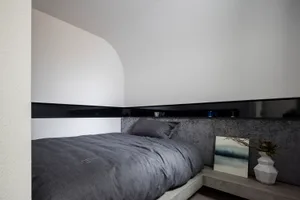 A modern minimalist bedroom with a grey upholstered bed on a concrete platform, illuminated by soft light and accented with a