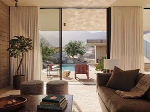 A modern minimalist living room with a large window, a comfortable sofa, and a view of a pool and mountains.