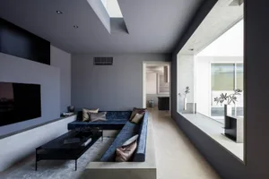 A minimalist living room with a concrete interior, featuring a sleek blue sofa and a flat-screen TV.