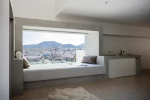 A minimalist living room with a concrete window seat, modern furnishings, and a view of the city and mountains.