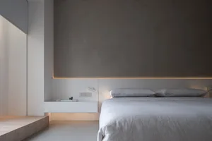 Minimalist bedroom featuring concrete headboard and white bedding, minimalistic design.