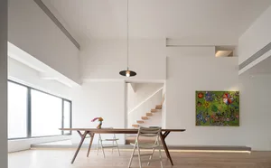Modern minimalist dining room featuring a wooden table and white chairs, with a green artwork hanging on the wall and a stair