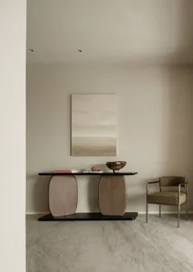 A minimalist living room featuring a console table with organic-shaped wood columns, a black tabletop, and a single brown cha