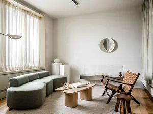 A modern minimalist living room featuring a gray upholstered sofa, wooden side tables, and glass wall decor.