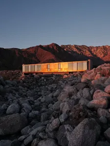 Modern house with metallic siding in a rocky desert landscape at sunset.