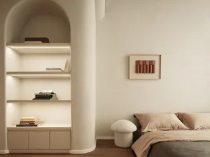 A minimalist bedroom with neutral-toned furniture and decor, featuring a bed with soft bedding and a curved shelf with books