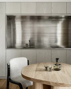 A minimalist modern kitchen with metallic finishes and a round wooden table.