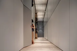 A modern corridor with glass panel walls and a wooden floor, featuring a minimalist design aesthetic.