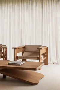 A minimalist living room featuring a wooden couch and table, with sheer white curtains in the background.