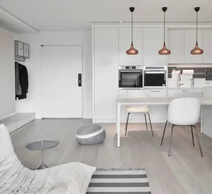 A minimalist living space featuring white furniture, pendant lights, and a modern kitchen area.