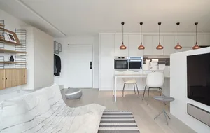 Modern kitchen with minimalist design, featuring white cabinets, appliances, and flooring, and a white dining area with chair