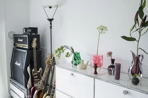 Minimalist music room featuring guitars, Marshall amplifiers, and decorative vases on a white cabinet.