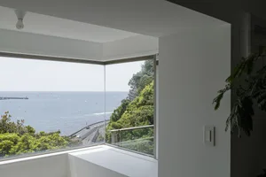 A modern residential window offers a glass view of the ocean and lush greenery.
