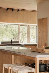 A modern kitchen interior with a concrete countertop and wooden stools.