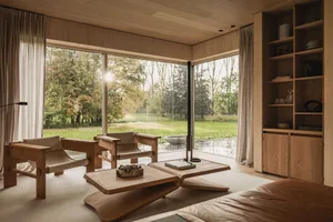 Modern minimalist living room with wooden furniture and large windows showing a scenic outdoor view.