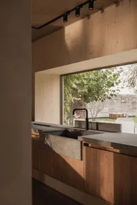 Modern kitchen with concrete sink, wooden cabinetry, and large window overlooking greenery.