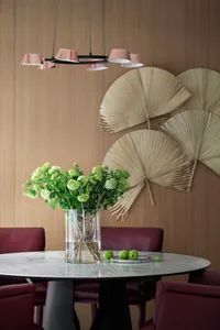 Modern dining room featuring a glass vase with flowers, leaves, and apples on a marble table with red chairs.
