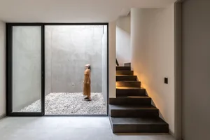 A modern minimalist concrete interior space with a person standing in a small gravel courtyard.