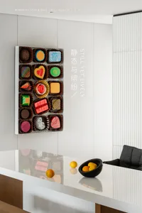 A well-designed minimalist interior featuring a sleek black table with oranges, a white counter with a black bowl of oranges,