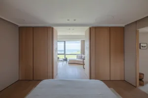 A modern minimalist bedroom with a wooden bed and wooden closet doors in front of a window with a view of the ocean.