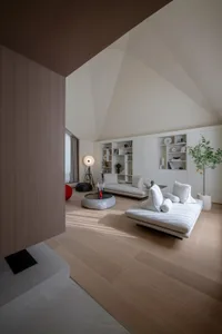 A minimalist living room with wood flooring, white furniture, and a high ceiling with exposed beams.