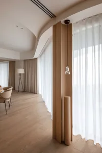 Contemporary living room featuring wooden columns, sheer curtains, and a neutral color palette.