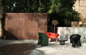 Outdoor lounge area featuring modern furniture, including a red armchair, green sculptural chair, and black sculptural chair,