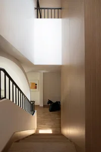 A modern staircase interior with wooden steps and black metal railings, featuring a wooden wall and a window.