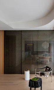 Modern minimalist living room featuring a black grid partition, wooden floor, and a single black and white cowhide chair.