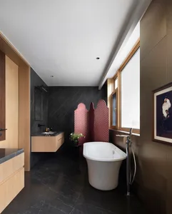 Modern bathroom with black marble walls and floor, white bathtub, red textile partition, and wooden cabinets.