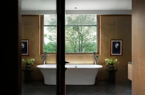 A clean, minimalist bathroom with a large white ceramic tub, framed by large windows and surrounded by brown walls.